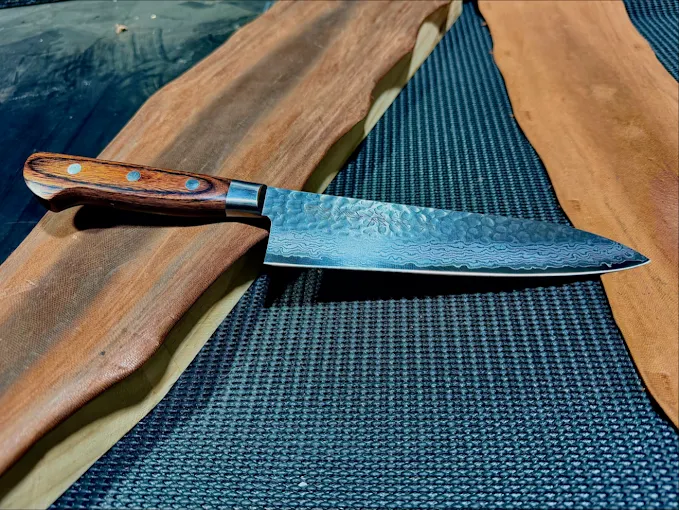 A Damascus steel chef's knife with timber handle, freshly sharpened on a live-edge board
