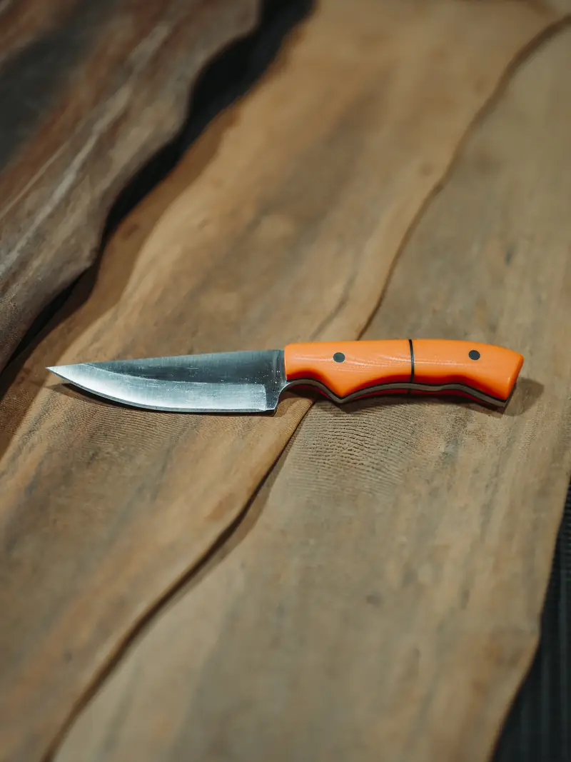 The Spiker in orange G10 with black liners and pins, and a hand-ground blade with a forged finish along the spine