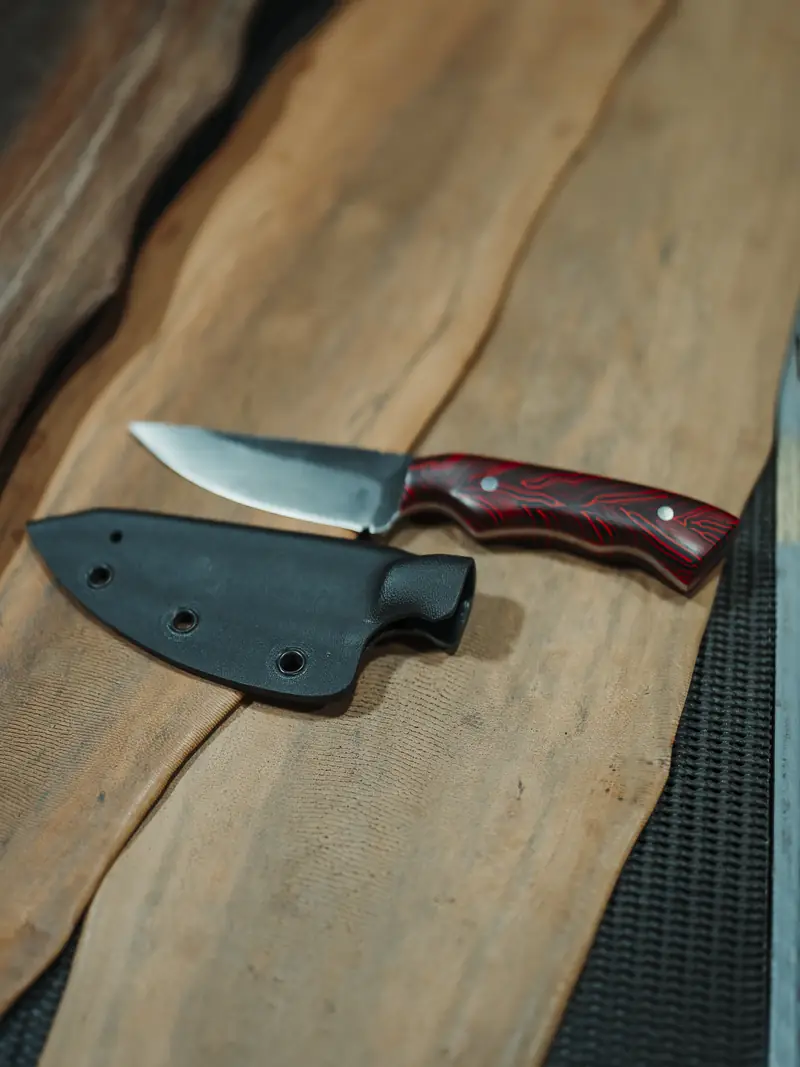 The Spiker drawn from its black kydex sheath, showing the satin finished blade and red G10 handle