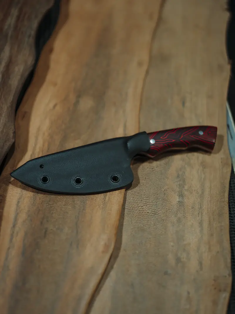 The Spiker seated in its moulded black kydex sheath with only the red G10 handle showing
