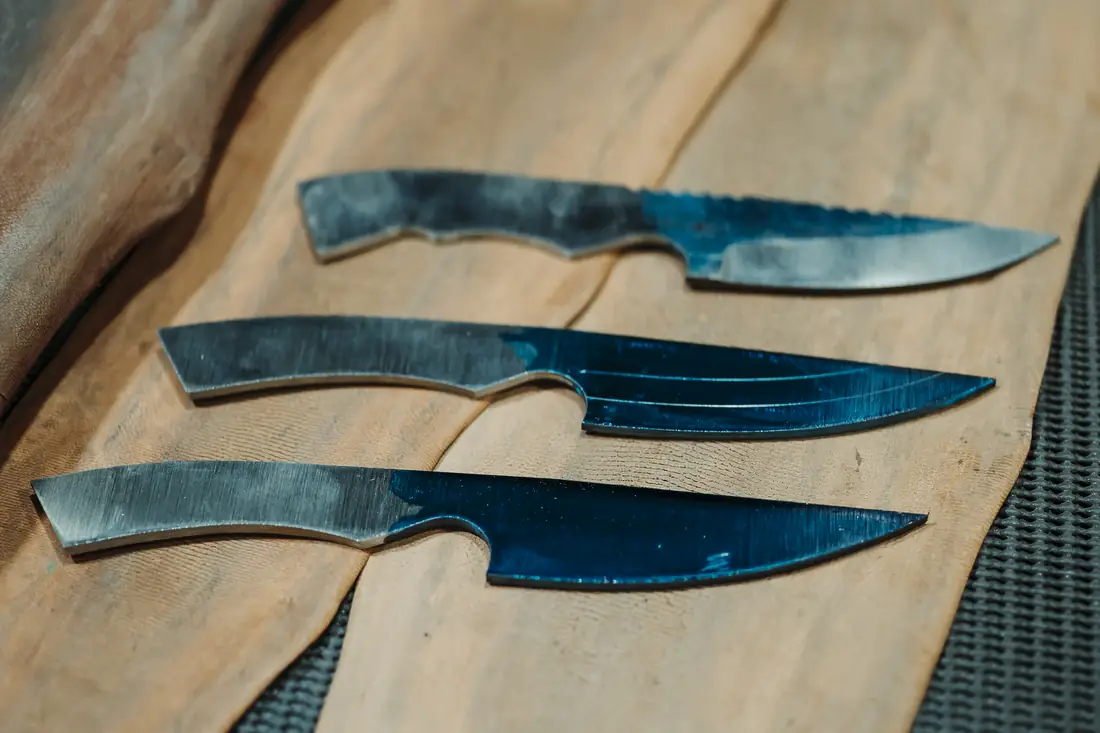 Three knife blanks on the bench: The Spiker rough ground at the top, and two Pickets below it with centrelines and bevel lines marked in blue engineering dye