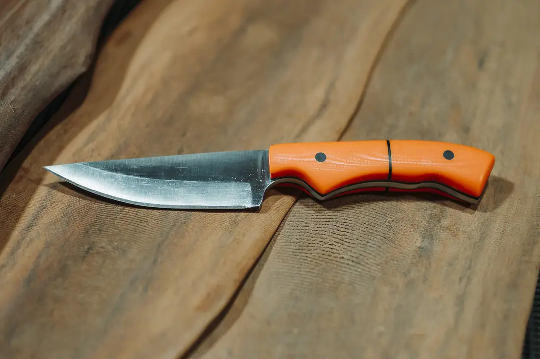 The Spiker in orange G10 with black liners and pins, blade ground by hand, on a timber slab
